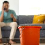 a living room with a bucket on the floor, catching a water leak from the ceiling