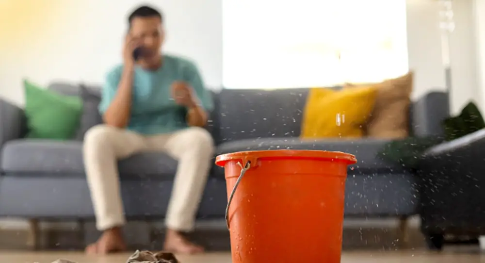 a living room with a bucket on the floor, catching a water leak from the ceiling