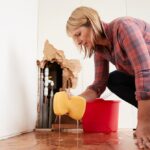 Worried woman mopping up water from a burst pipe with sponge