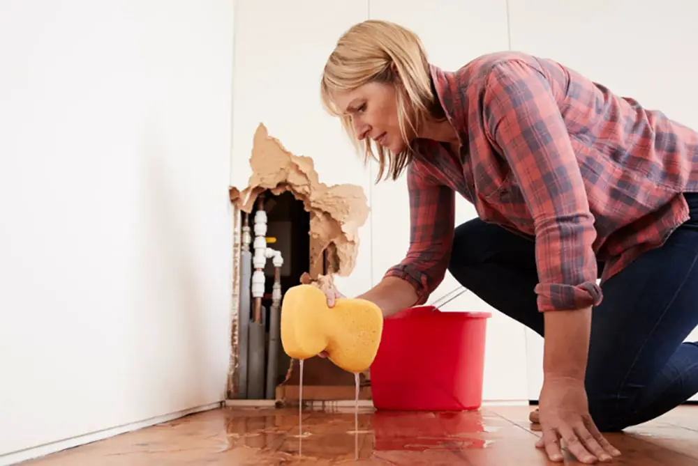 Worried woman mopping up water from a burst pipe with sponge